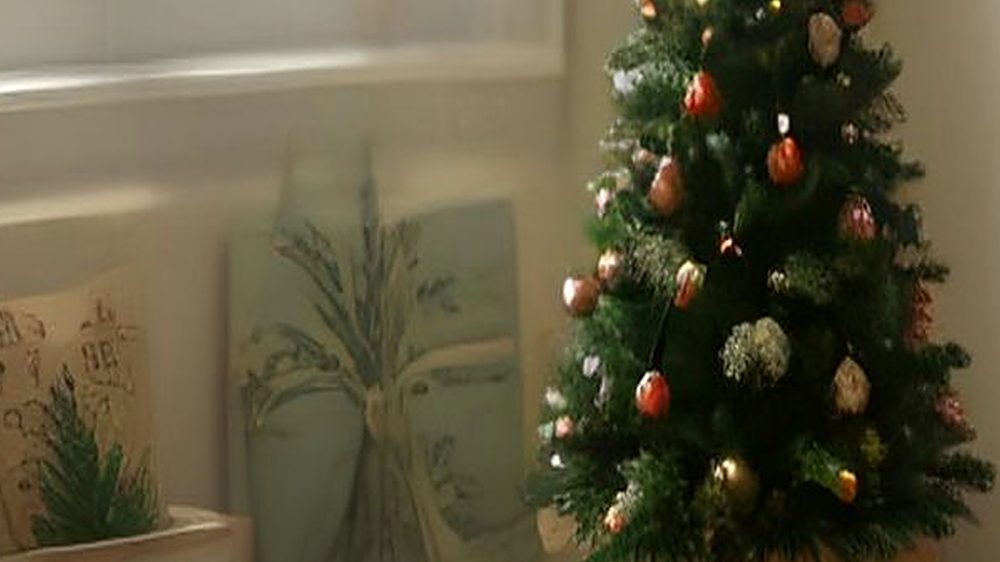 A cozy home office desk decorated for Christmas with a small tree, lights and candles